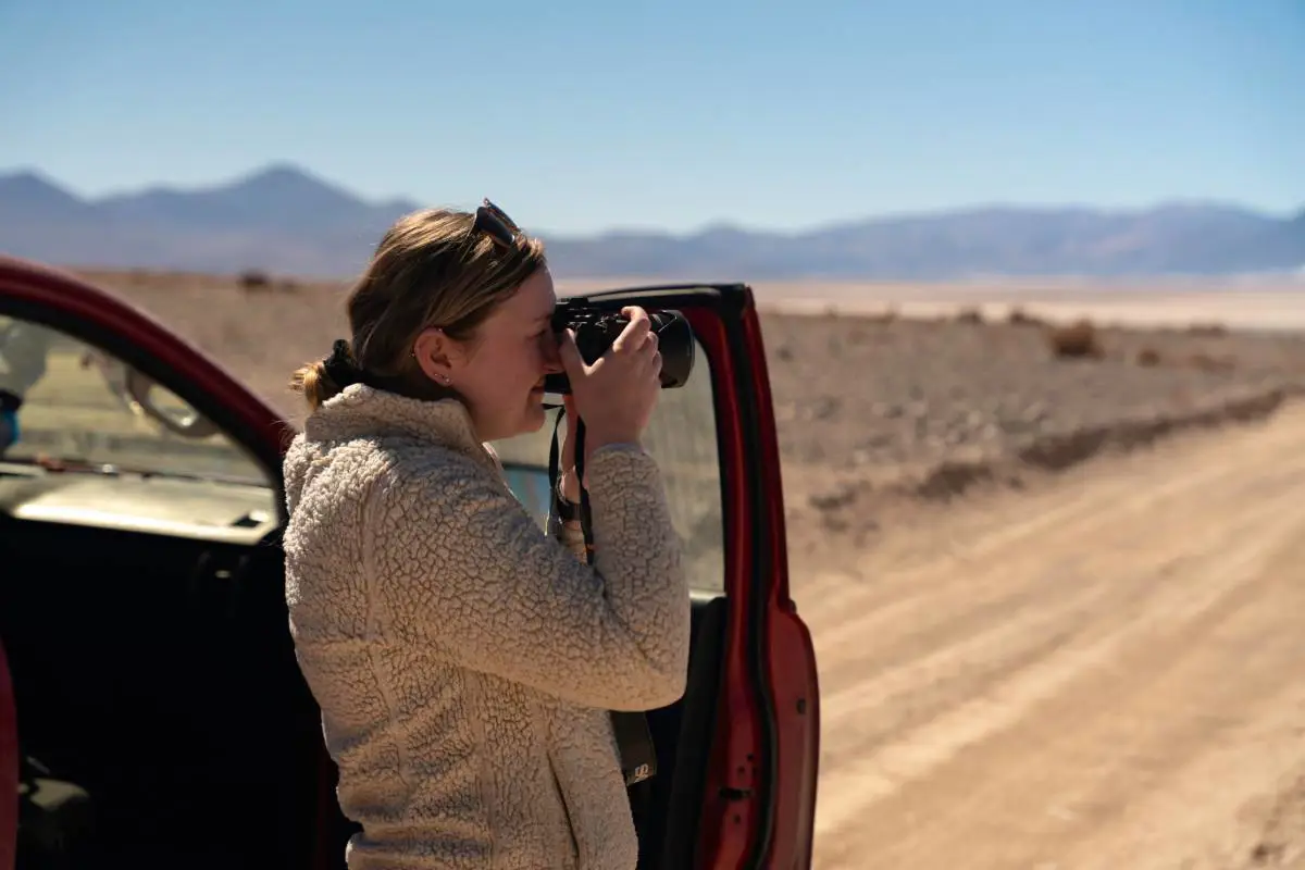 Becca Marsh standing next to the passenger door of her car in the Atacama desert taking a photo of wildlife. Photo by Alex Keefe.