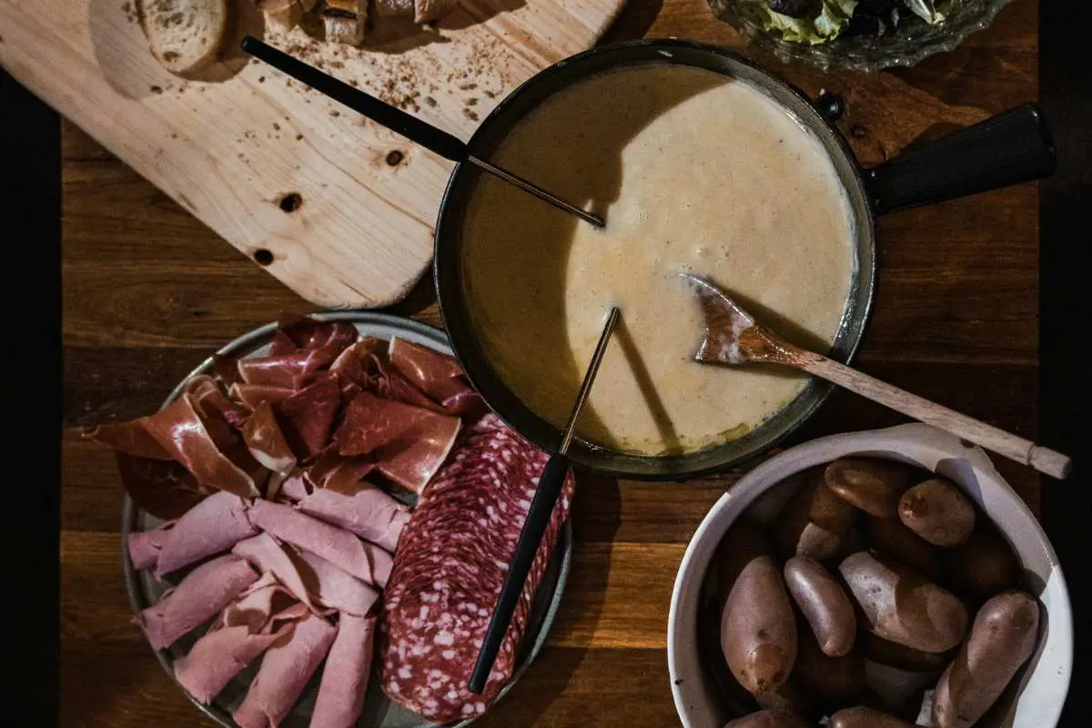 Top down view of cheese fondue, meats And vegetables on rustic table. Photo By Yann Allegre, Unsplash.