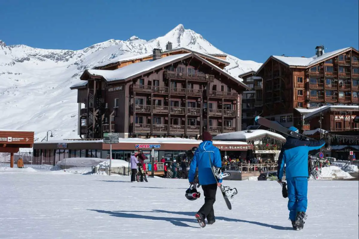 A snowboarder and skier walk towards the Intersport ski shop in Tignes le Lac France. Photo by Valentin de Brabandere from Unsplash