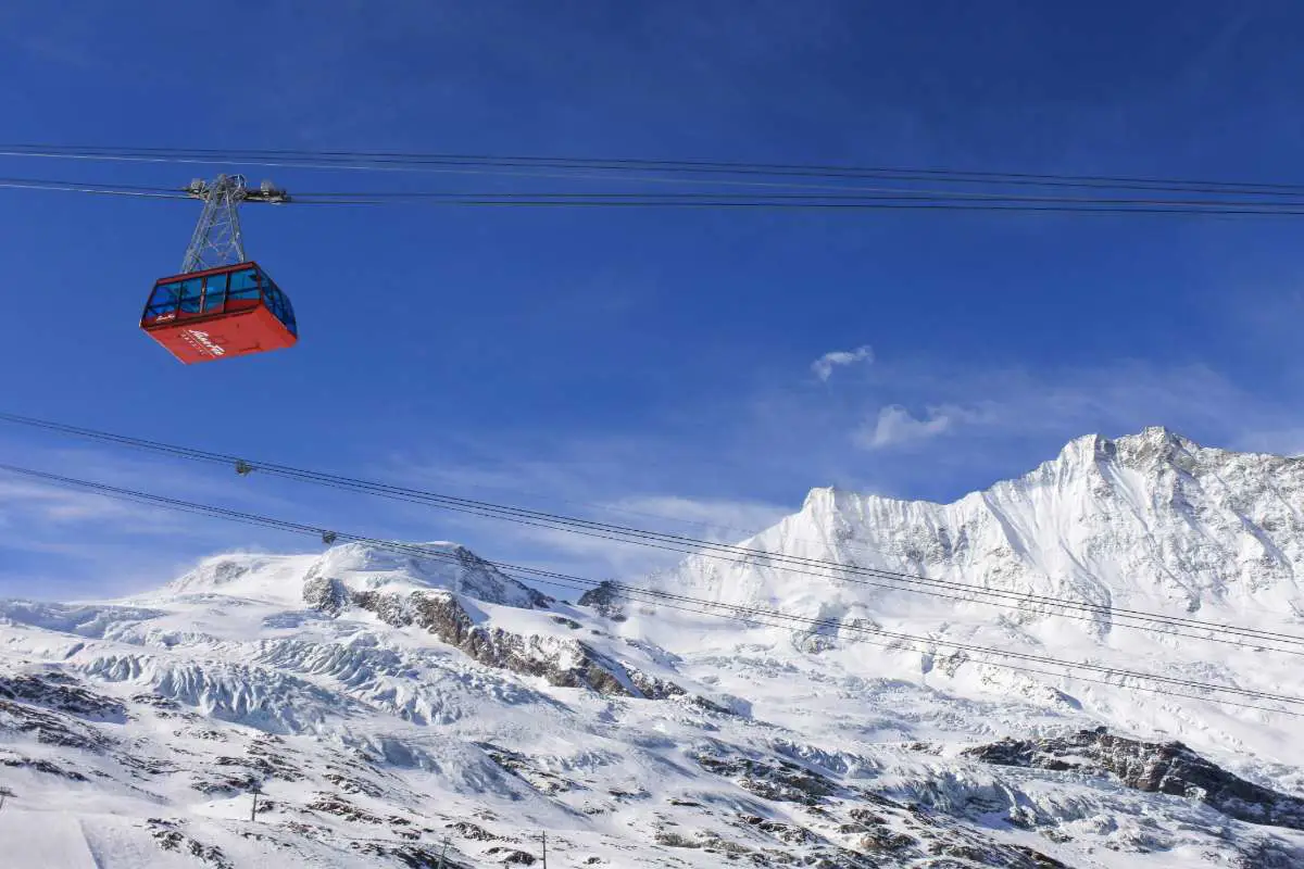 Felskin cable car in Saas Fee, Switzerland with a snowy backdrop and blue skies. Photo by Corey Catracho from Unsplash