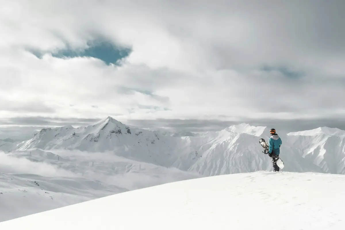 A lone snowboarder stands at the top of the piste ready to make a descent at Les Menuires, France. Photo by Yann Allegre from Unsplash