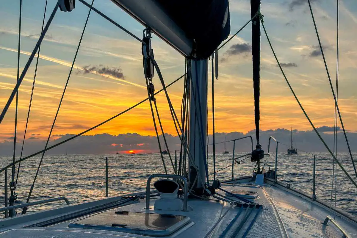 A sailing boat sets out to sea at sunrise with the sun just coming above the horizon with six silhouettes of other sailing boats.. Photo By Becca Marsh