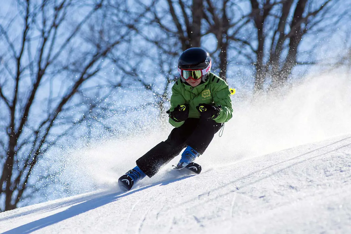 Skifahrerjunge in grüner Jacke fährt bergab. Foto von Pexels, Pixabay.