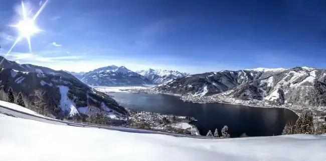 Blick von oben auf einen Bergsee im Winter mit verschneiten Bergen