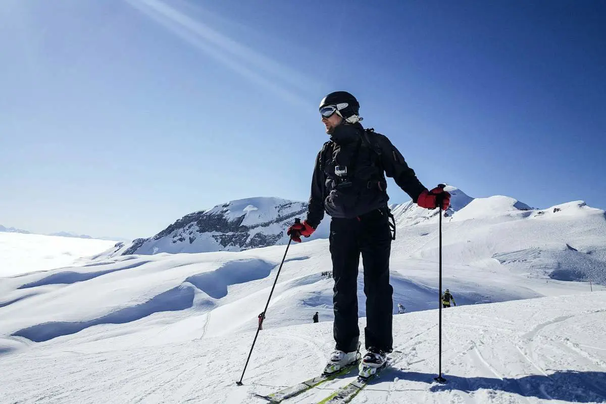 Homme à ski en milieu de piste, sous un ciel bleu clair, admirant la vue sur les montagnes enneigées de la station de ski de Flaine, en France. Photo de Kasya Shahovskaya sur Unsplash.