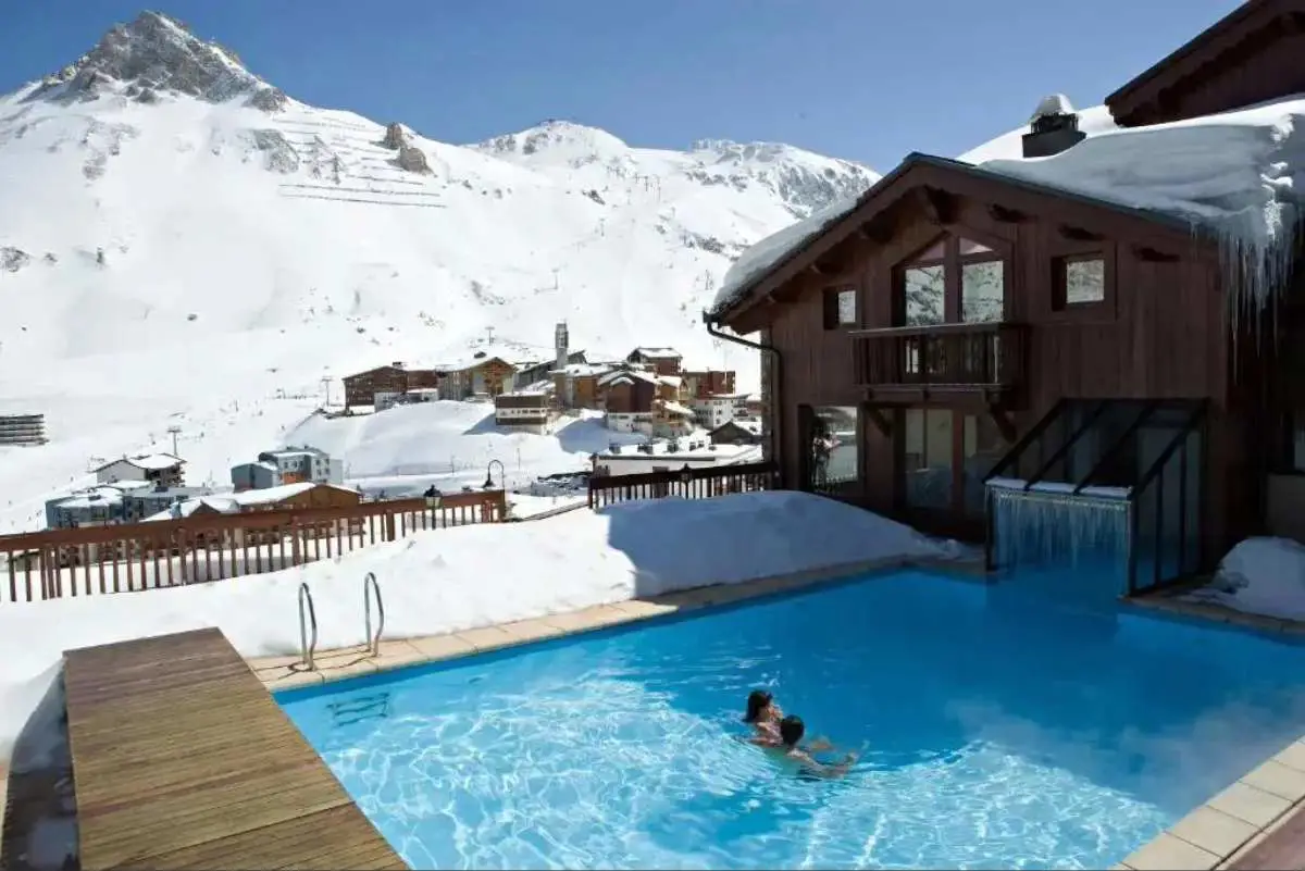 Outdoor swimming pool at Hôtel Village Montana by Les Etincelles overlooking the snow capped mountains at Tignes ski resort France.
