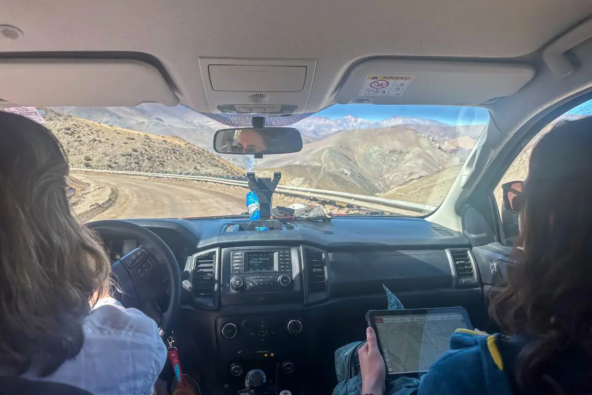 View from inside a car through the windscreen of dry desert mountains and a winding road. Photo by Becca Marsh.