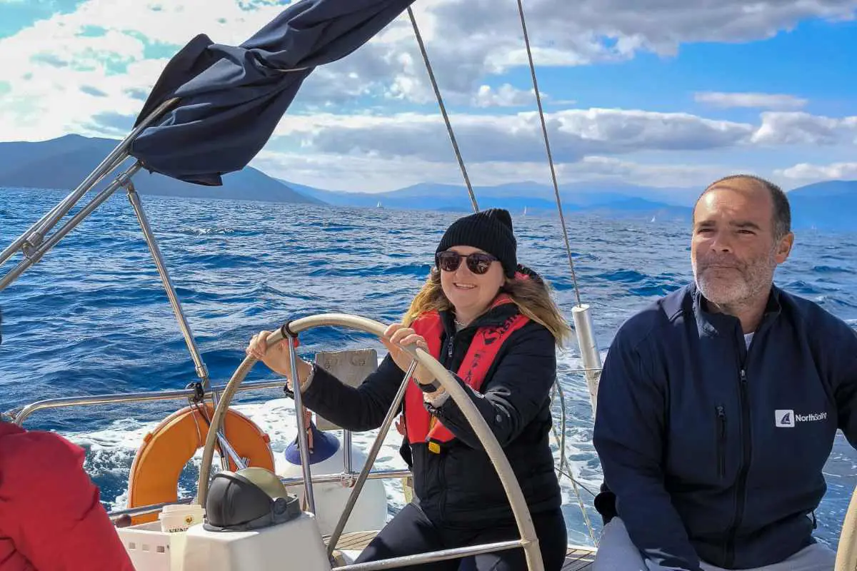 Sailing student sitting at the helm learns how to steer alongside captain on sailing flotilla in Greece. 