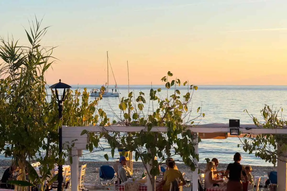 View from a beach side restaurant in Greece watching a sail boat glide by at sunset.