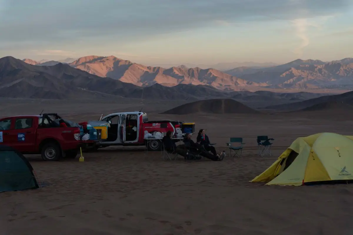 Three people sit around camp with two tents and two cars in the Dunes of Copiapo in the Atacama Desert Chile. Photo by Alex Keefe.