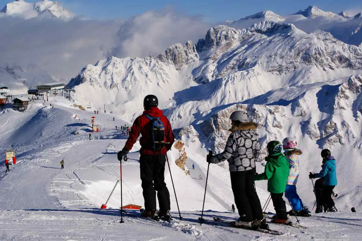 Family of 4 standing together on a piste ready to head down together at Courchevel ski resort, France. Photo by Piotr Figlarz from Unsplash