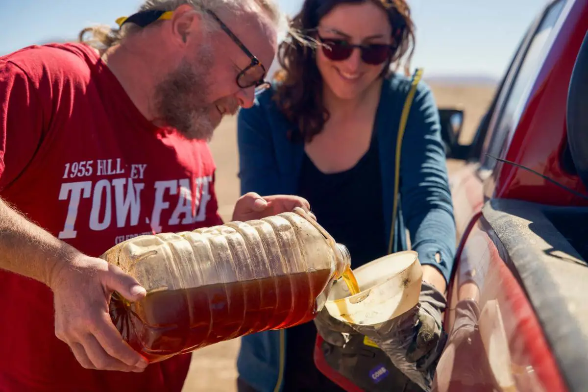 A man and woman pour recycled cooking oil into the fuel tank of a car to mix with diesel. Photo by Becca Marsh.