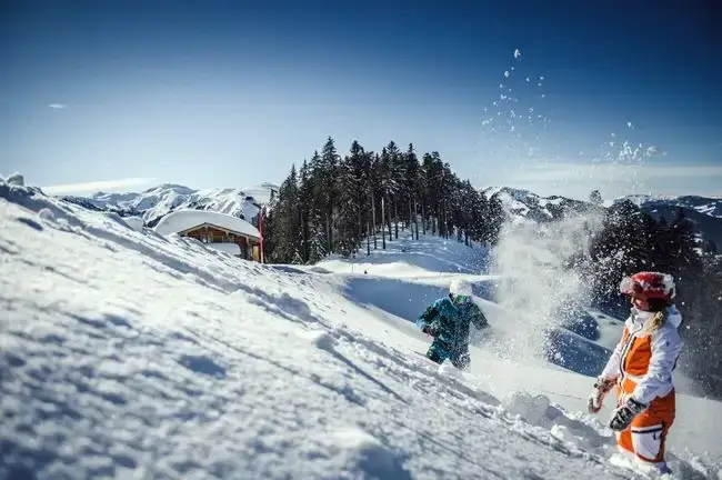 Mann Frau mit Skikleidung spielt mit Schnee auf einer Piste