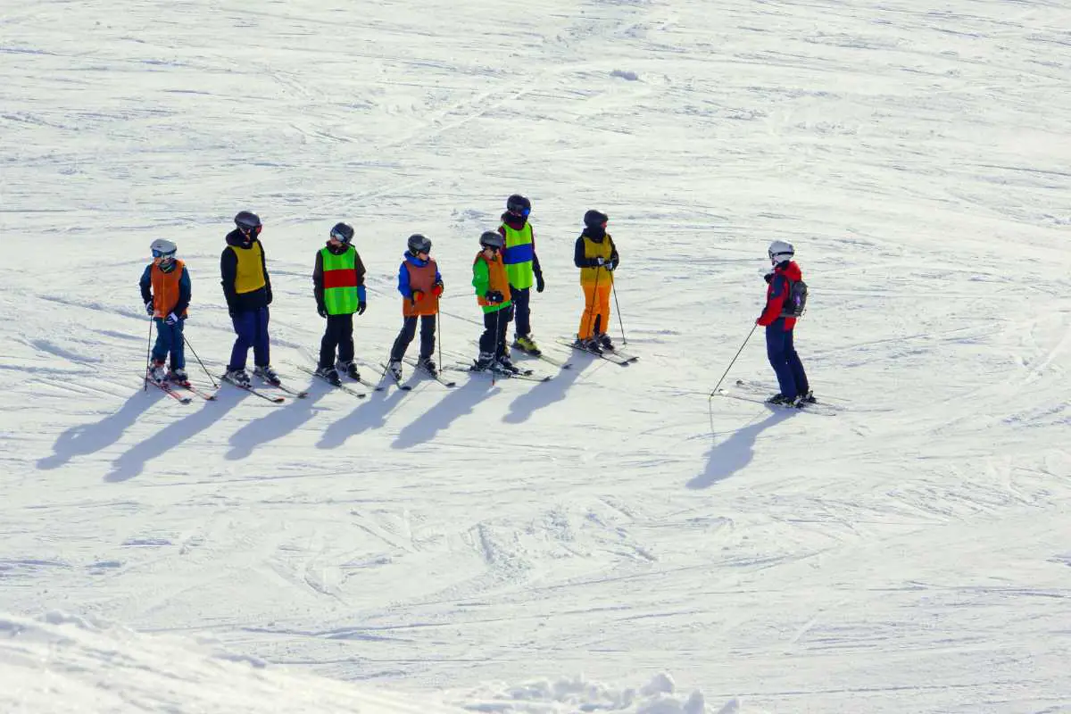Six Children Lined Up On The Ski Slope In Front Of Instructor Learning How To Ski. Photo By Boris Misevic, Unsplash.